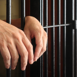 prisoner behind bars.hand of prisoner on steel jail bars.Man under arrested by policeman because illegal behaviour.