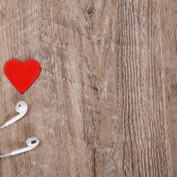 White headphones with red heart. Love listening music. Sound earphones lying on wooden rustic background.